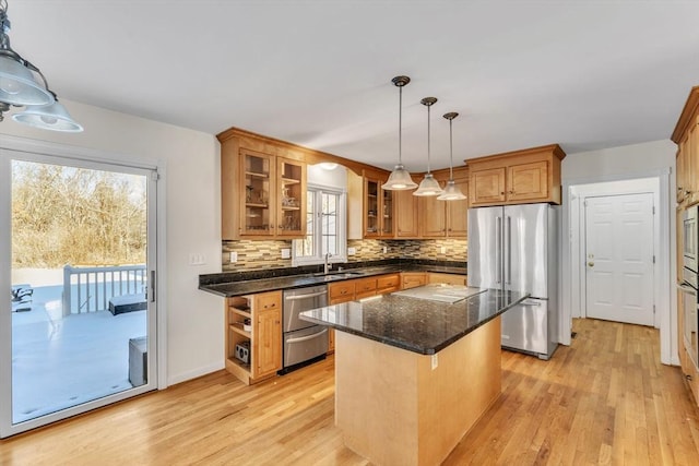 kitchen featuring a sink, appliances with stainless steel finishes, a center island, decorative light fixtures, and glass insert cabinets