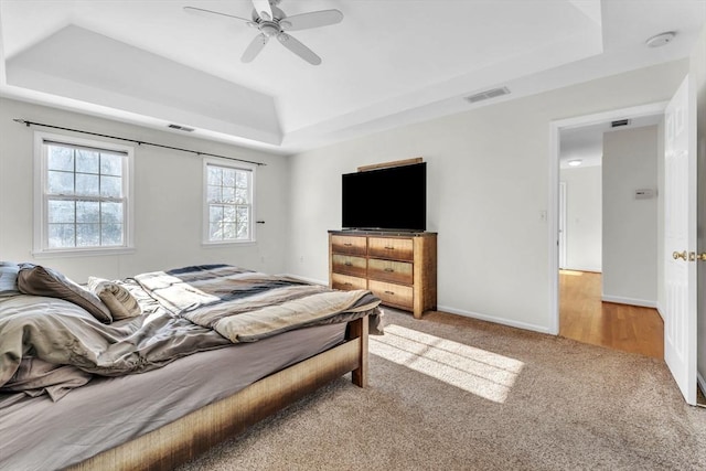 carpeted bedroom featuring a raised ceiling, visible vents, ceiling fan, and baseboards