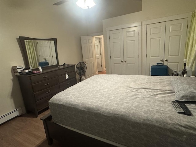 bedroom with a baseboard heating unit, multiple closets, and wood finished floors