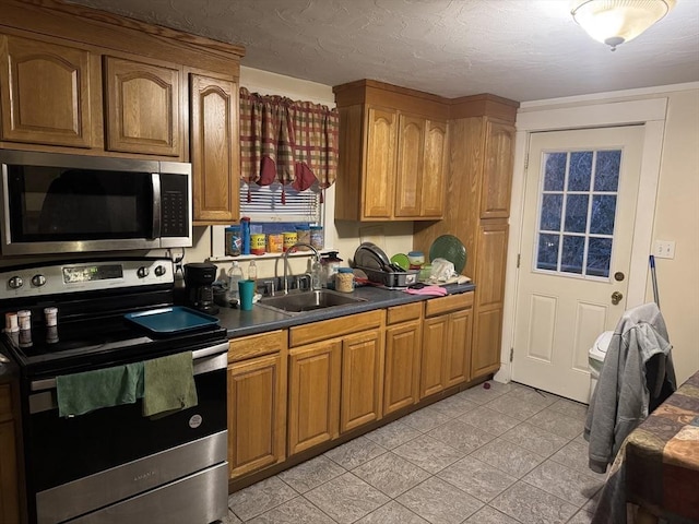 kitchen featuring dark countertops, appliances with stainless steel finishes, brown cabinetry, and a sink