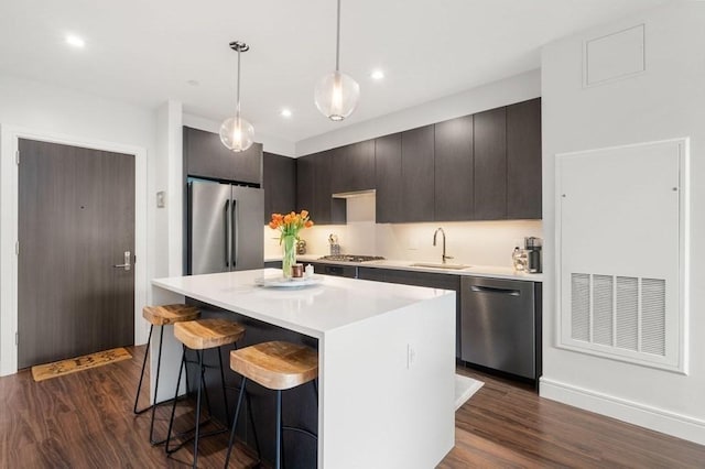 kitchen with dark wood finished floors, a center island, light countertops, stainless steel appliances, and a sink