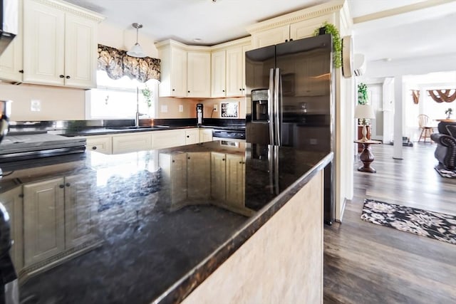 kitchen with wood finished floors, cream cabinets, dark stone counters, decorative light fixtures, and a sink