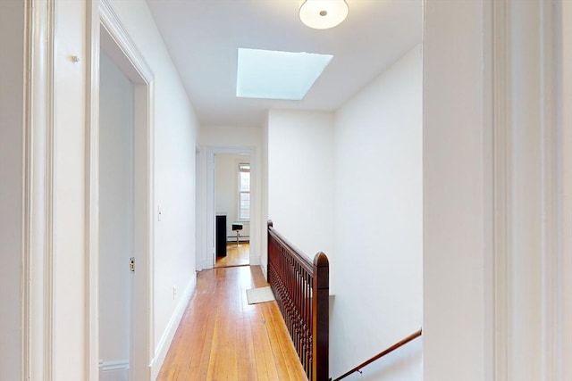 hall featuring baseboard heating, a skylight, and light wood-type flooring