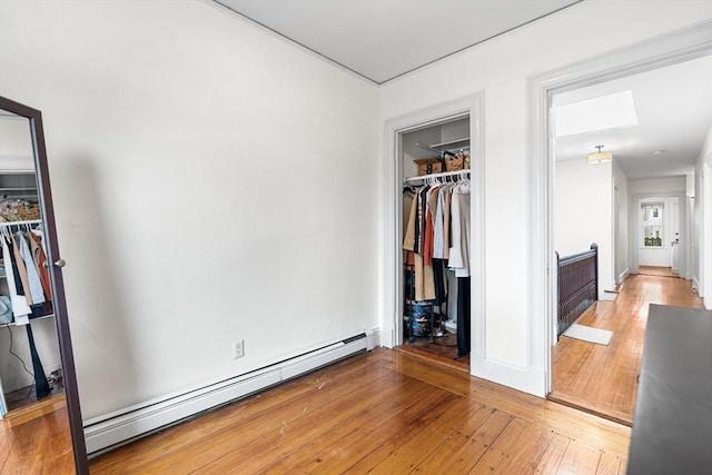 bedroom featuring a baseboard radiator, a walk in closet, light wood-type flooring, and a closet