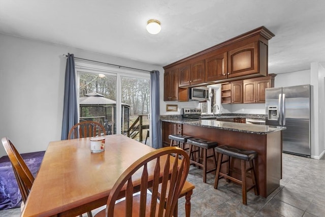 kitchen with a sink, open shelves, a breakfast bar area, appliances with stainless steel finishes, and dark stone counters
