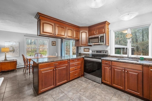 kitchen with a sink, stainless steel appliances, brown cabinetry, and a peninsula