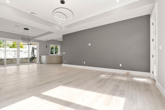 unfurnished living room with light hardwood / wood-style flooring, plenty of natural light, a tray ceiling, and a chandelier