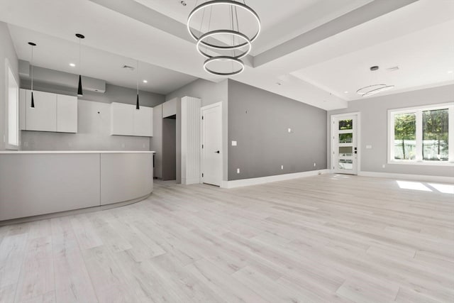 unfurnished living room with light wood-type flooring, a chandelier, and a tray ceiling