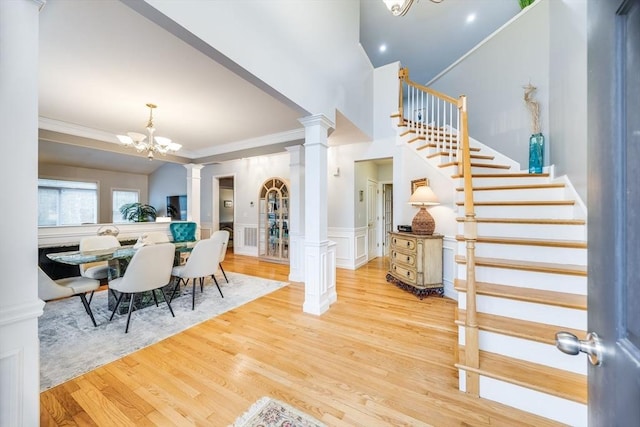 foyer entrance featuring ornate columns, wood-type flooring, crown molding, and an inviting chandelier