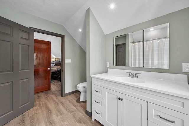 bathroom with hardwood / wood-style flooring, vanity, toilet, and vaulted ceiling