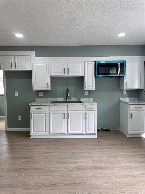 kitchen with a sink, stainless steel microwave, a textured ceiling, white cabinets, and light countertops