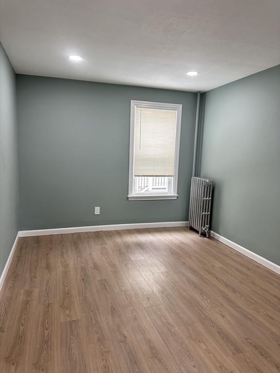 unfurnished room featuring radiator heating unit, wood finished floors, baseboards, and recessed lighting