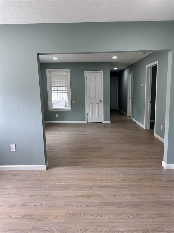 spare room with light wood finished floors, baseboards, and a textured ceiling