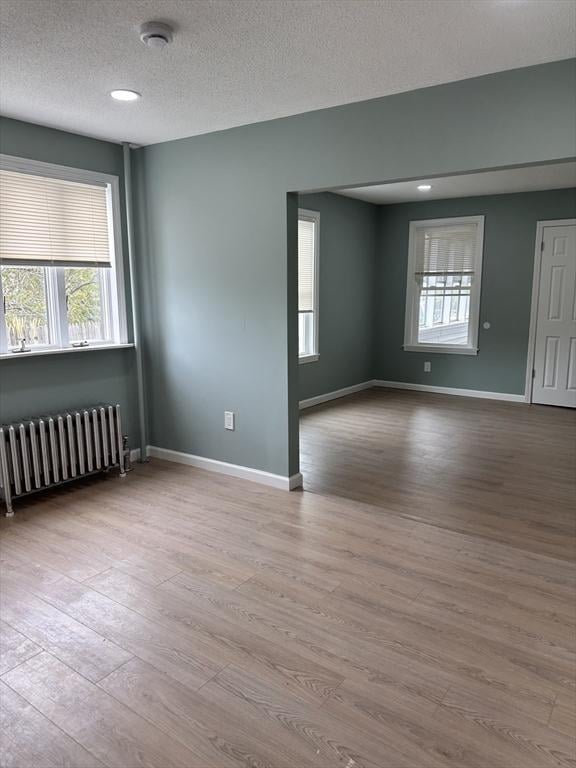 unfurnished room featuring radiator heating unit, wood finished floors, a smoke detector, baseboards, and a textured ceiling