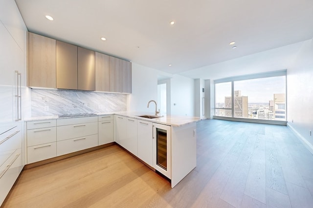 kitchen with light hardwood / wood-style floors, white cabinetry, wine cooler, kitchen peninsula, and decorative backsplash