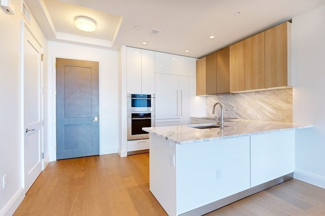 kitchen with white cabinets, sink, light stone counters, and kitchen peninsula