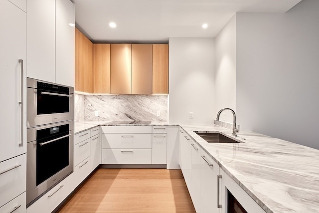 kitchen featuring light hardwood / wood-style floors, light stone counters, sink, tasteful backsplash, and white cabinetry