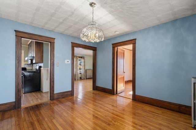 empty room featuring wood-type flooring, a chandelier, and radiator heating unit