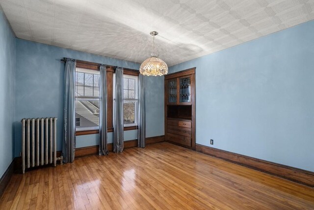 empty room featuring radiator heating unit, wood-type flooring, and a notable chandelier