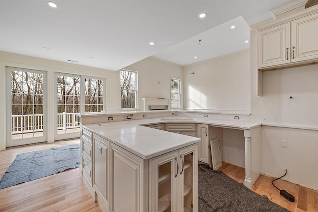 kitchen featuring recessed lighting, a kitchen island, light wood-style floors, ornamental molding, and light stone countertops