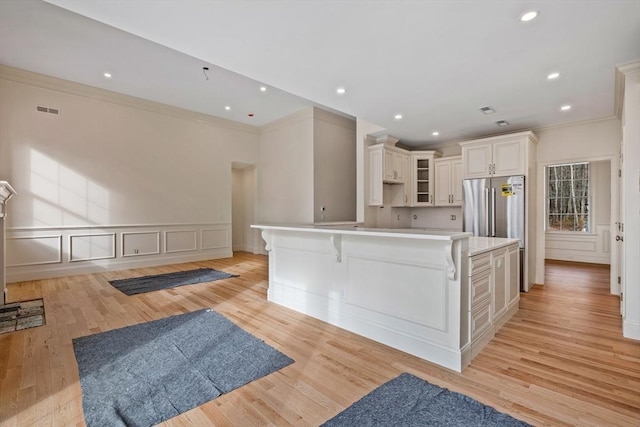 kitchen featuring light wood finished floors, visible vents, a large island, glass insert cabinets, and freestanding refrigerator