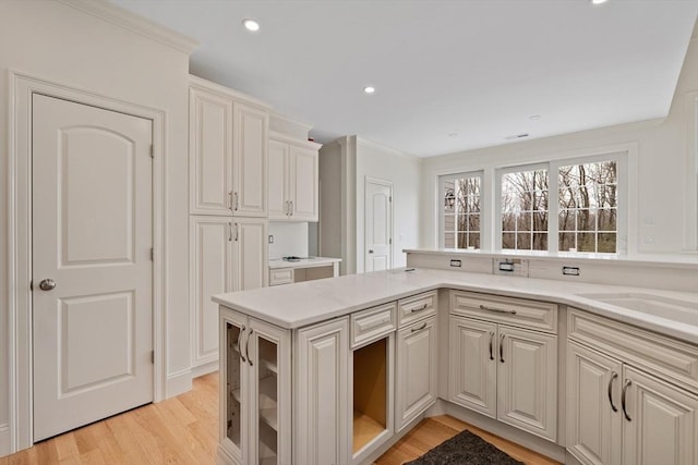 kitchen with recessed lighting, a sink, light countertops, light wood-type flooring, and crown molding