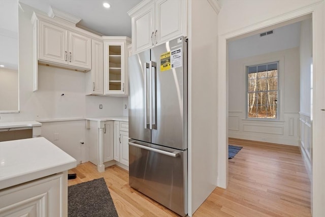 kitchen with visible vents, white cabinets, high quality fridge, glass insert cabinets, and light wood-type flooring