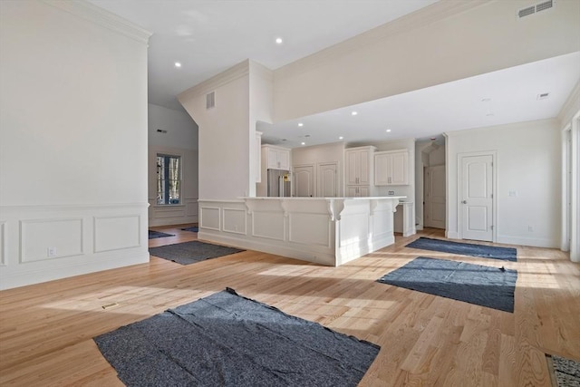 living room featuring wainscoting, visible vents, crown molding, and light wood finished floors