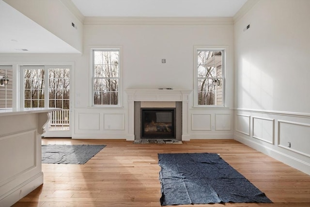 unfurnished living room featuring a wainscoted wall, a decorative wall, ornamental molding, a glass covered fireplace, and light wood-type flooring