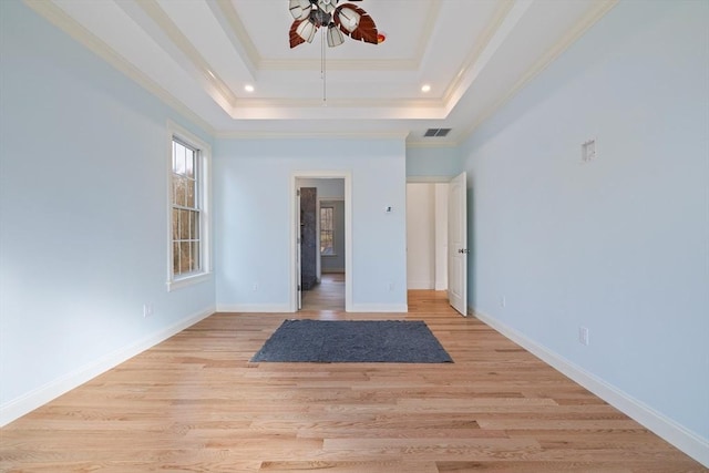 spare room featuring visible vents, baseboards, ornamental molding, light wood finished floors, and a raised ceiling