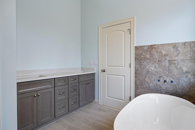 full bath featuring a freestanding bath, wood finished floors, vanity, and tile walls