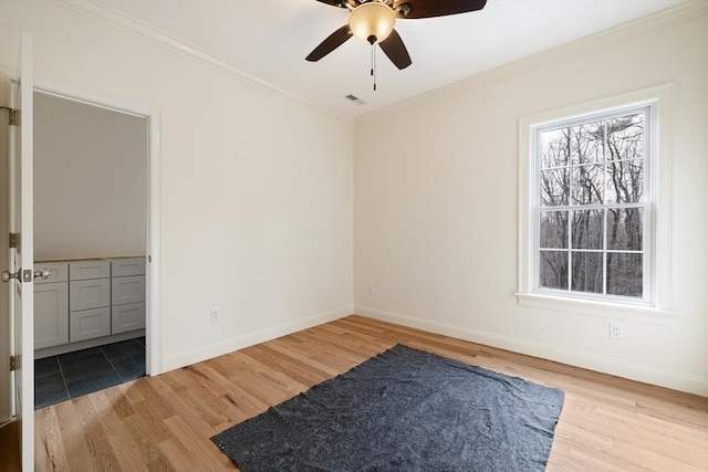 empty room with light wood-style floors, crown molding, and baseboards