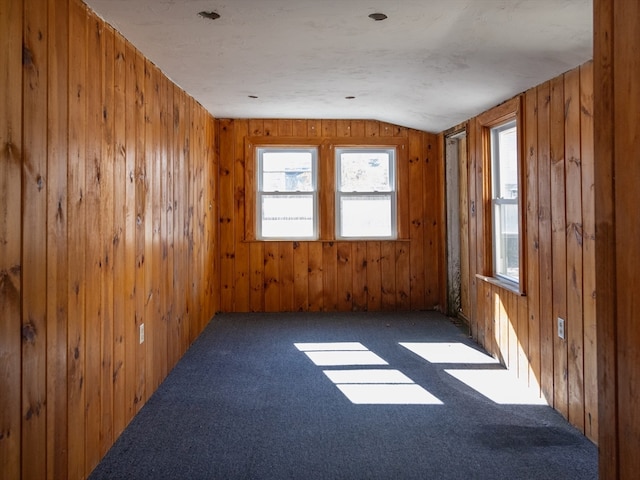 spare room featuring lofted ceiling, wood walls, and dark colored carpet