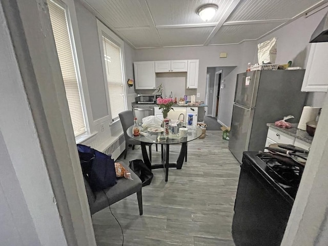 kitchen with ventilation hood, light hardwood / wood-style flooring, appliances with stainless steel finishes, radiator heating unit, and white cabinets