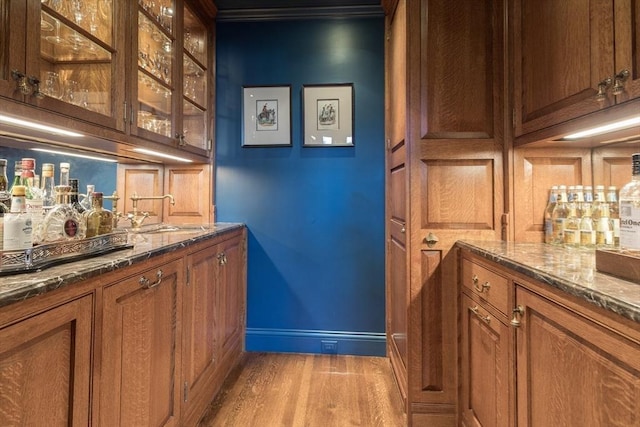 bar with sink, light hardwood / wood-style flooring, and dark stone counters