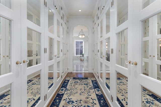 corridor featuring french doors, ornamental molding, wood-type flooring, and a high ceiling