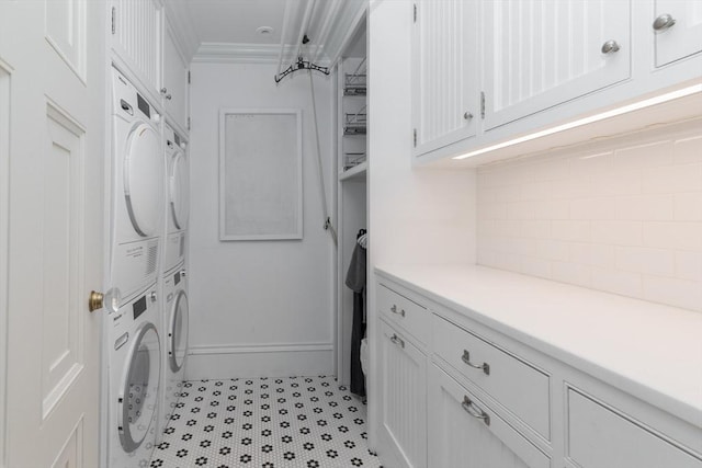 clothes washing area with ornamental molding, cabinets, and stacked washing maching and dryer