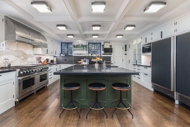 kitchen with white cabinetry, a kitchen island, built in appliances, and wall chimney exhaust hood