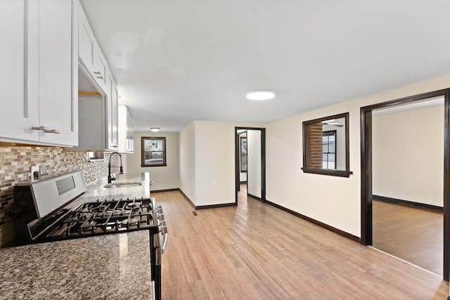 kitchen with sink, white cabinetry, light wood-type flooring, stainless steel gas range, and stone countertops