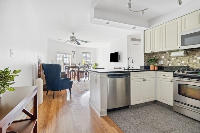 kitchen featuring a sink, tasteful backsplash, dark countertops, stainless steel appliances, and a peninsula