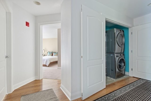 washroom with laundry area, baseboards, stacked washer / drying machine, and light wood finished floors