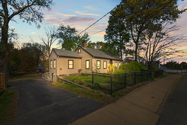 bungalow-style home featuring a chimney, a fenced front yard, and aphalt driveway