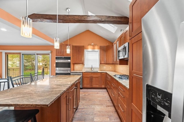 kitchen with brown cabinets, appliances with stainless steel finishes, a kitchen breakfast bar, light wood-style flooring, and lofted ceiling with skylight