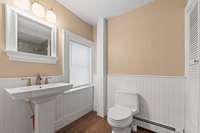 bathroom with a sink, wood finished floors, toilet, a wainscoted wall, and a baseboard radiator