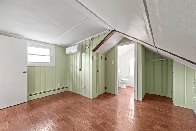 bonus room featuring a wall unit AC, baseboard heating, lofted ceiling, and hardwood / wood-style floors