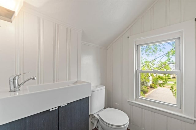 bathroom featuring toilet, vaulted ceiling, ornamental molding, and a decorative wall