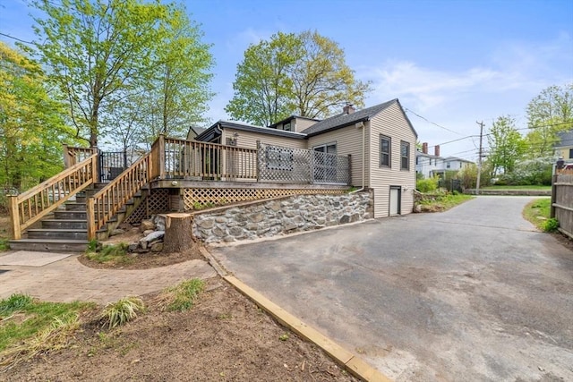 back of property featuring a deck, driveway, a chimney, and stairs