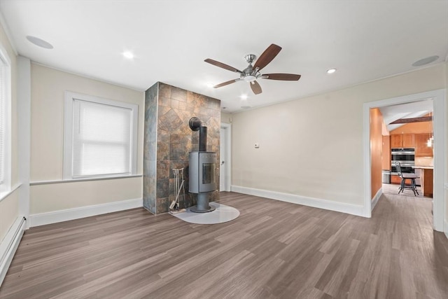 unfurnished living room with wood finished floors, a wood stove, a ceiling fan, and a baseboard radiator