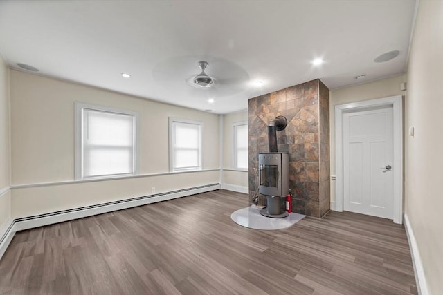 unfurnished living room featuring baseboards, ceiling fan, a wood stove, and wood finished floors