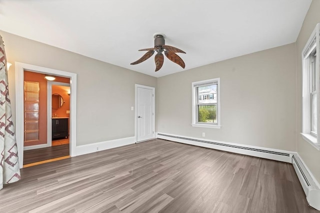 spare room with a ceiling fan, a baseboard heating unit, and wood finished floors